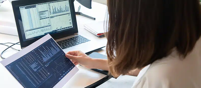 A worker sat at a desk with a laptop looking at a data print out reviewing KPIs and metrics of an employee wellbeing strategy