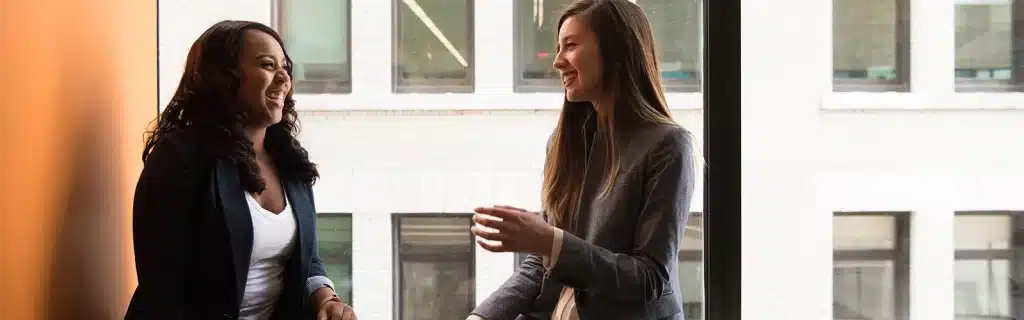 Two female colleagues in a workplace laugh while discussing activities for World Mental Health Day