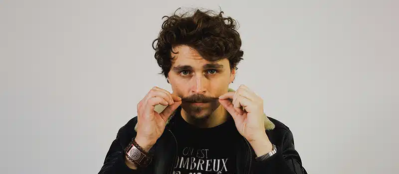 A man with dark hair grooming his moustache
