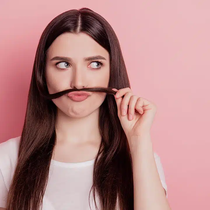 A woman holding her hair over her lip like a mustache, celebrating movember in the workplace