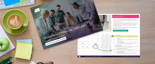 The Workplace Wellbeing Calendar on a desk next to a cup of coffee and a selection of stationery.