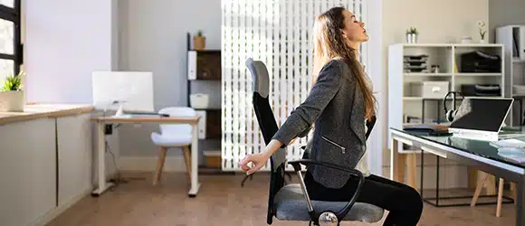 A woman stretching at her desk as pat of a desk yoga routine