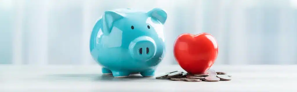 A piggy bank and a red heart on a pile of coins, representing financial wellbeing