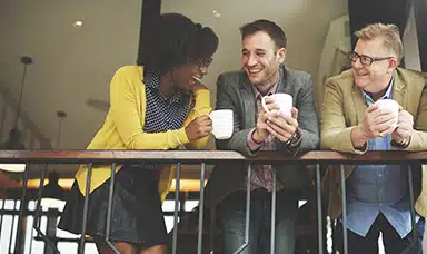 A group of three managers holding coffee cups, talking and smiling.