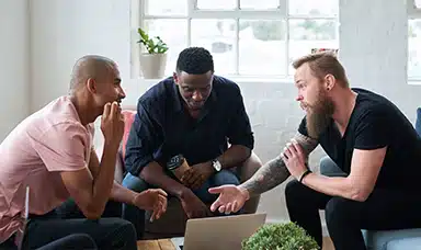Three men sitting around a desk talking.