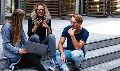 A group of young people sitting on a set of stairs talking and using a laptop