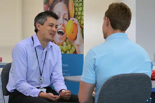 A man talking to a New Leaf Health practitioner whilst holding a piece of cotton on his finger, taking part in an Employee Health Screening