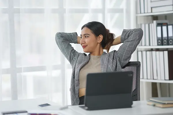 A relaxed and resilient woman in an office sits at her desk with her hands behind her head after taking part in stress and resilience training