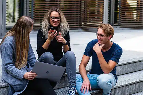A group of colleagues sitting on stairs outside of an office building talking and smiling