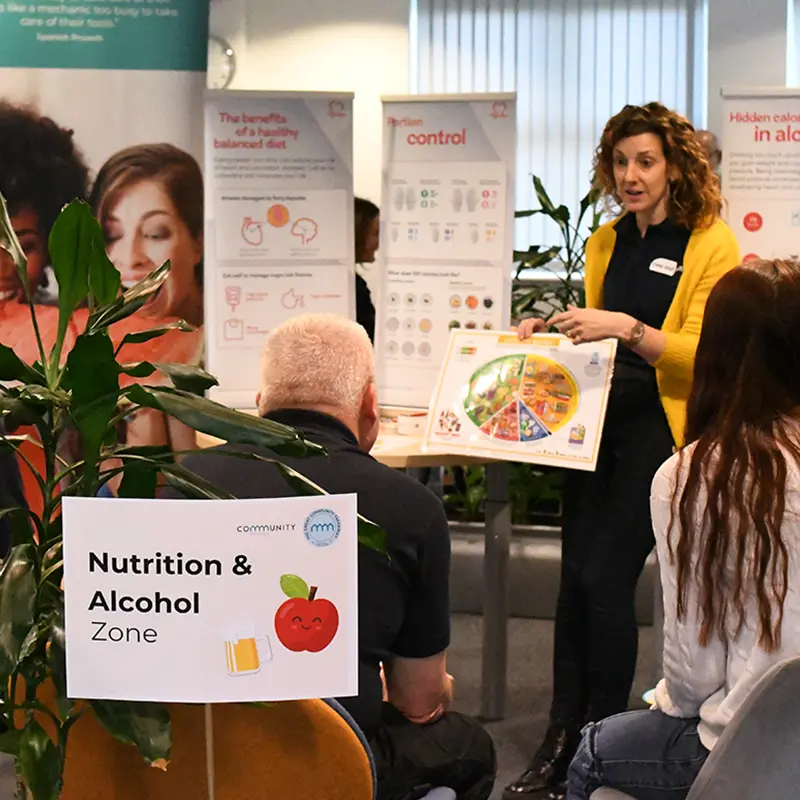 A New Leaf Health practitioner discussing nutrition and alcohol with a group of employees at a workplace Health Fair