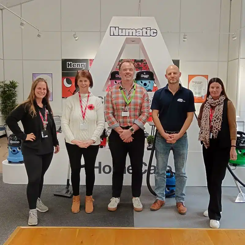 A group of employees standing in front of the Numatic logo with a New Leaf Health wellbeing practitioner