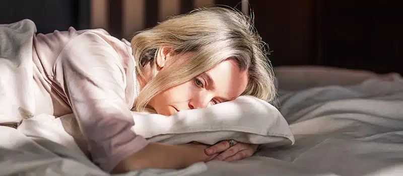 An ill woman lying in bed having not participated in a workplace flu clinic