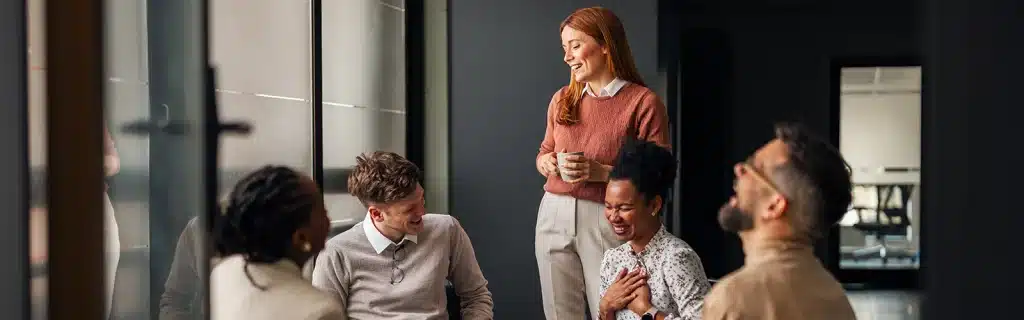 A group of employees sitting and smiling in a workplace showcasing positive workplace wellbeing