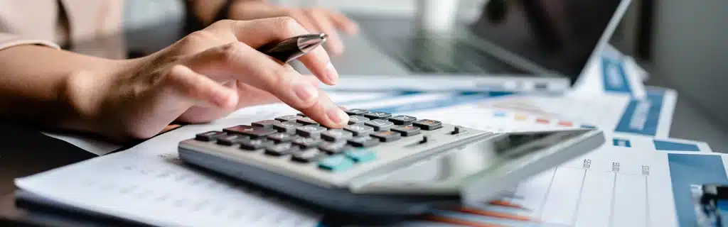 A woman using a calculator on a desk calculating a workplace wellbeing programme cost