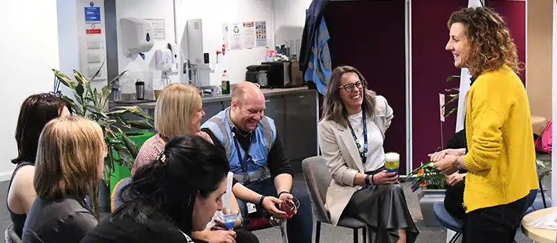 A group of employees engaging with a wellbeing practitioner, showcasing an efficient workplace wellbeing programme cost