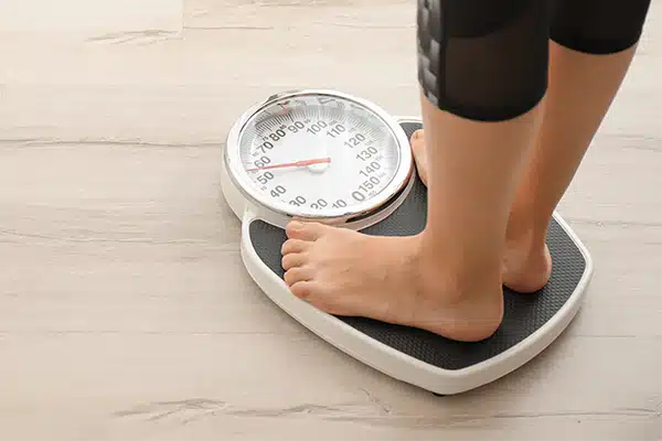 A woman standing on a set of scales used to calculator bodyweight, helping to calculate basal metabolic rate.
