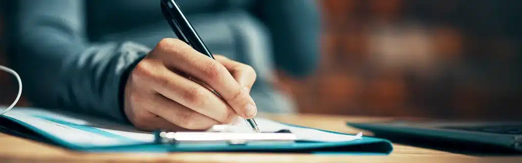 An employee writing on a piece of paper on a clipboard completing an employee wellbeing survey