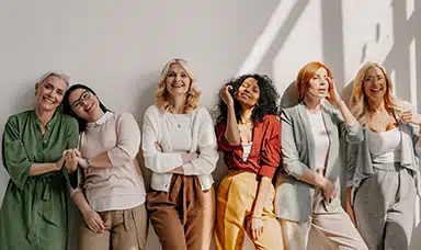 A group of women smiling at the camera leaning against a wall, showcasing menopause support in the workplace