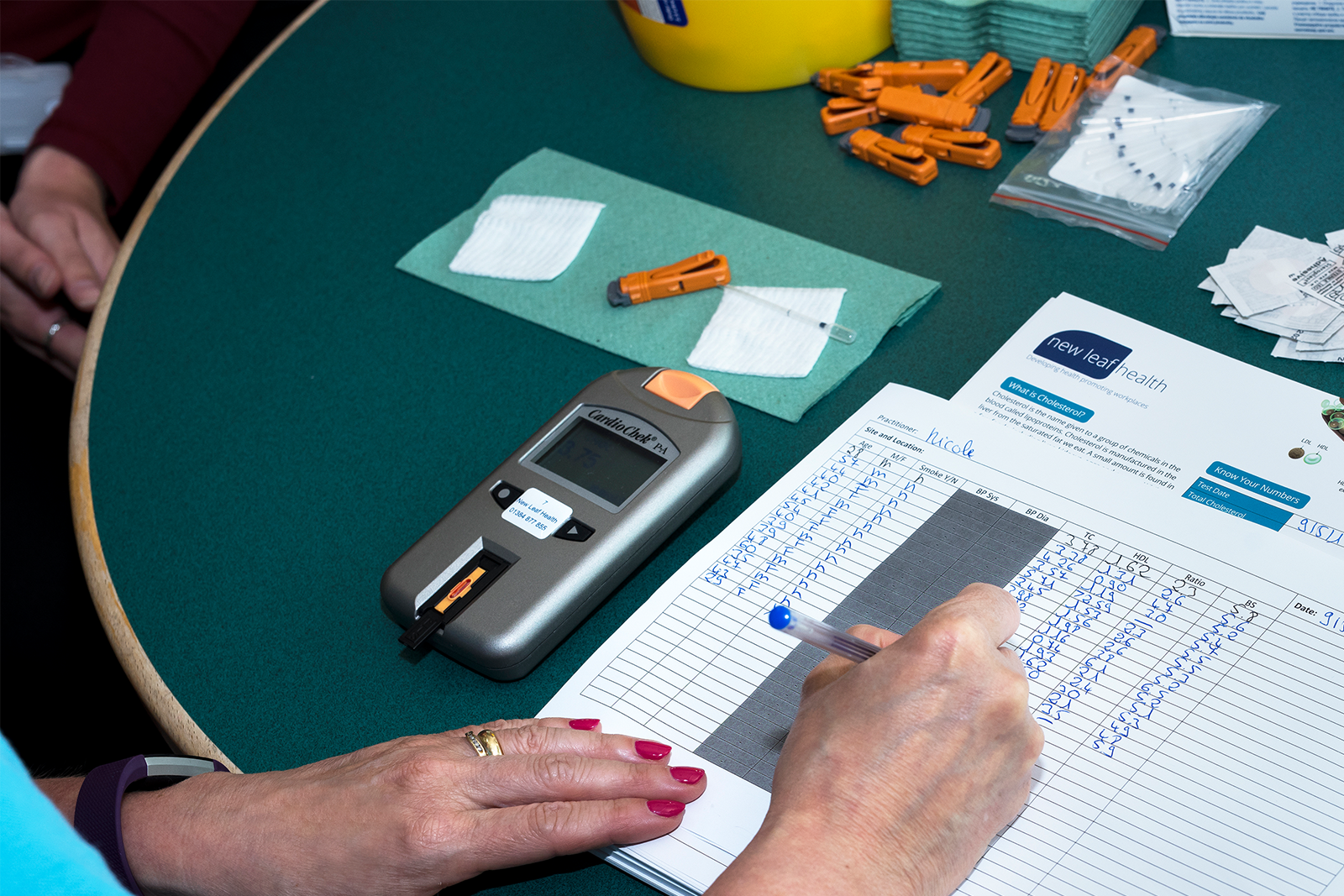 A New Leaf Health practitioner writing out results with the employee health screening equipment layed out of the table