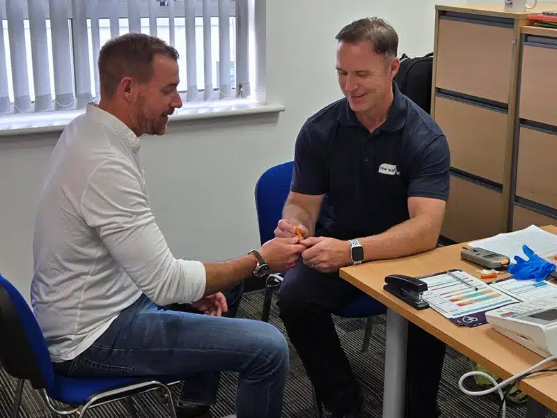 An attendee taking part in a finger-prick test with a New Leaf Health practitioner during an employee health screening