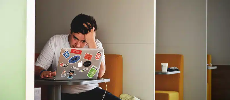 A man sitting in a co-working space on his laptop, looking frstradedly at the screen, illustrating the need for preventing burnout in the workplace